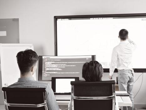 A colleague sketches a diagram on a whiteboard while developers work at a monitor